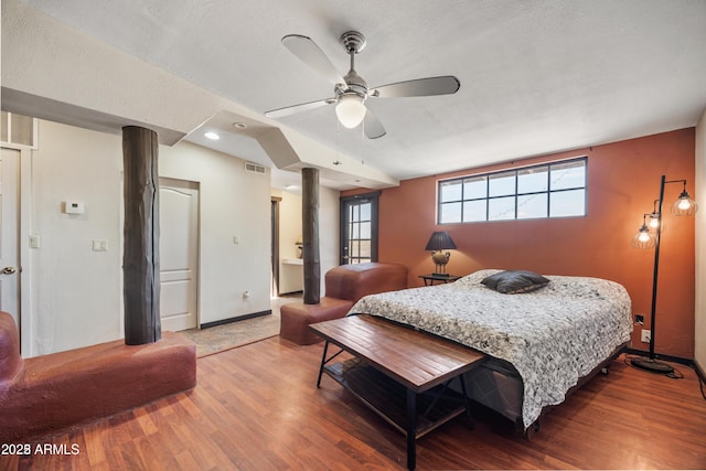 bedroom with a textured ceiling, visible vents, baseboards, wood finished floors, and a ceiling fan