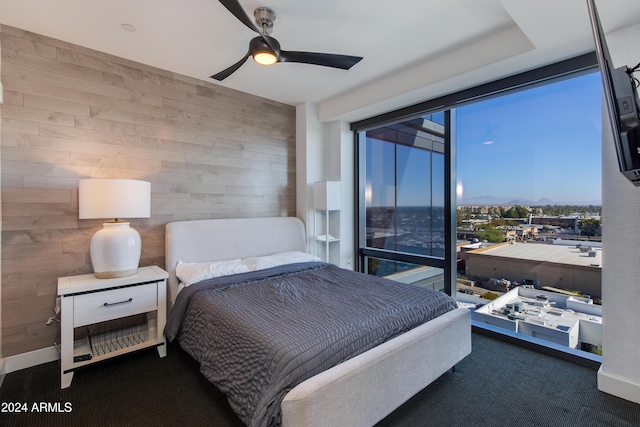 bedroom with ceiling fan, wooden walls, and dark colored carpet