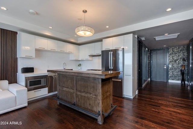 kitchen featuring stainless steel appliances, dark hardwood / wood-style floors, decorative light fixtures, white cabinets, and a center island