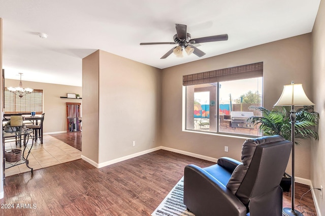 living area featuring wood-type flooring and ceiling fan with notable chandelier