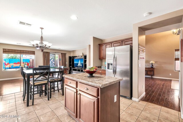 kitchen featuring pendant lighting, light wood-type flooring, a chandelier, a kitchen island, and stainless steel fridge