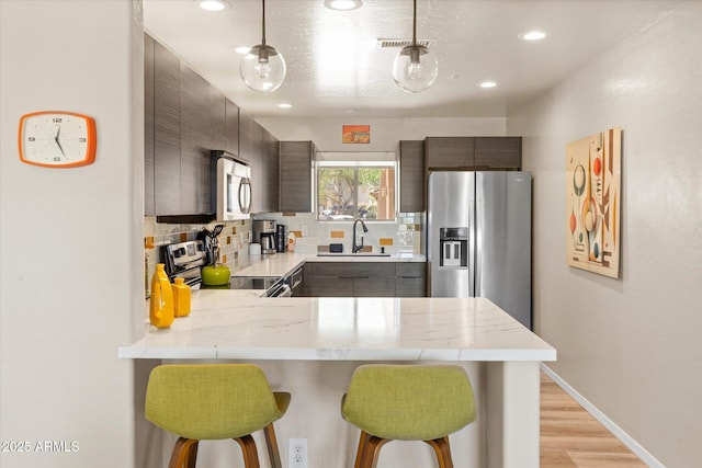19700 N 76th St Unit 1038, Scottsdale, AZ 85255 - kitchen with stainless steel appliances, a peninsula, a kitchen bar, tasteful backsplash, and light wood finished floors