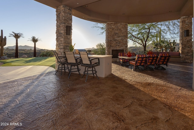 patio terrace at dusk featuring an outdoor bar, a mountain view, and an outdoor stone fireplace