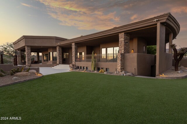 back house at dusk with a patio area and a lawn