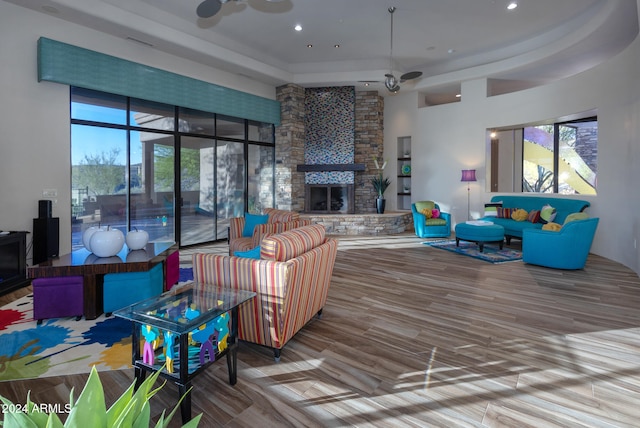 living room featuring ceiling fan, hardwood / wood-style flooring, a tray ceiling, a fireplace, and a towering ceiling