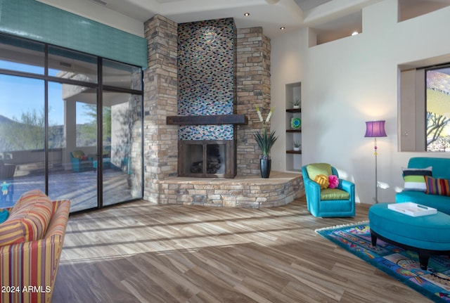 living room with a towering ceiling, a stone fireplace, and wood-type flooring