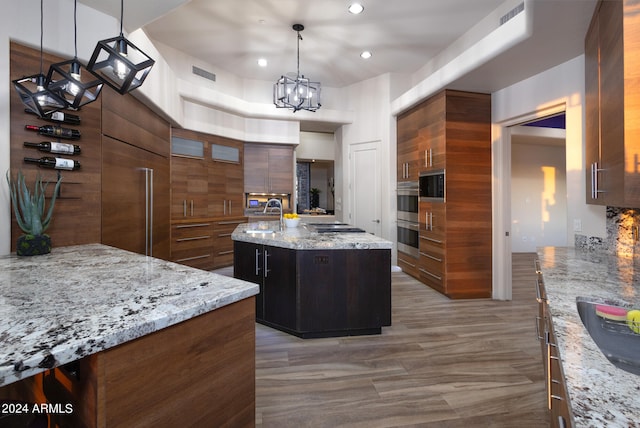 kitchen with a kitchen island, decorative backsplash, light stone countertops, pendant lighting, and an inviting chandelier