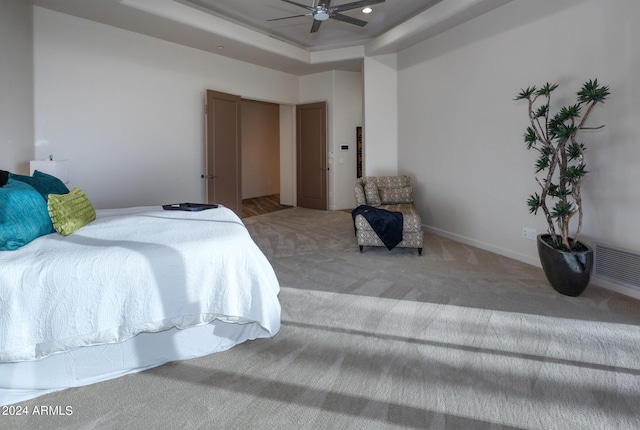 carpeted bedroom with ceiling fan and a tray ceiling