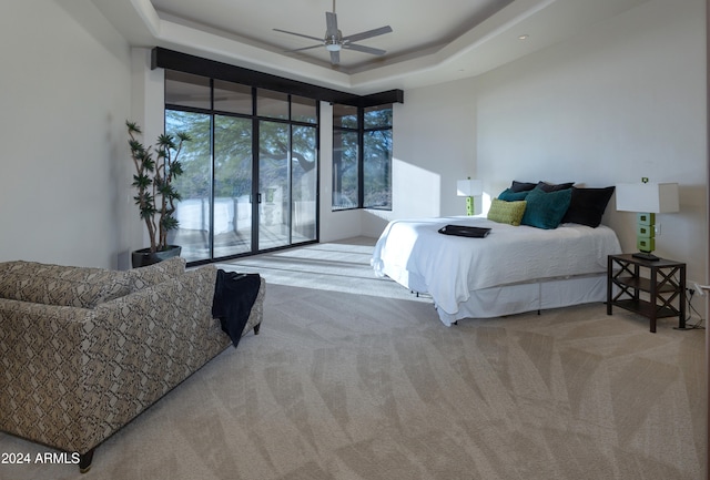 bedroom with ceiling fan, access to outside, a tray ceiling, a high ceiling, and light colored carpet