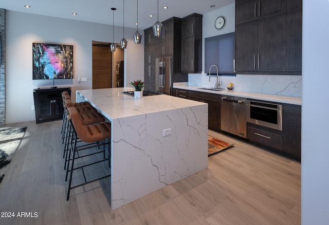 kitchen with light wood-type flooring, stainless steel appliances, sink, pendant lighting, and a center island