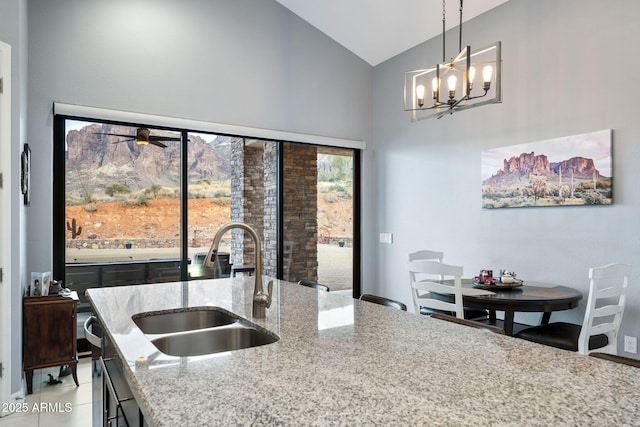 kitchen featuring sink, light stone counters, high vaulted ceiling, pendant lighting, and ceiling fan with notable chandelier