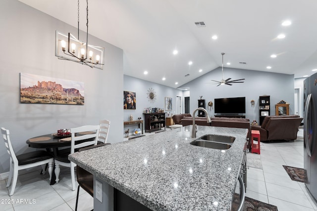 kitchen featuring sink, a kitchen breakfast bar, hanging light fixtures, light stone countertops, and a center island with sink