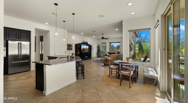 kitchen featuring stainless steel built in fridge, dark stone counters, hanging light fixtures, light tile patterned flooring, and ceiling fan