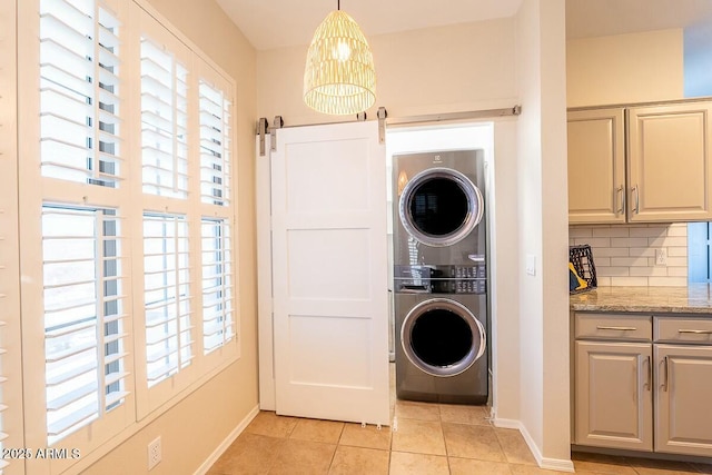 laundry room featuring a barn door, light tile patterned floors, and stacked washer and clothes dryer