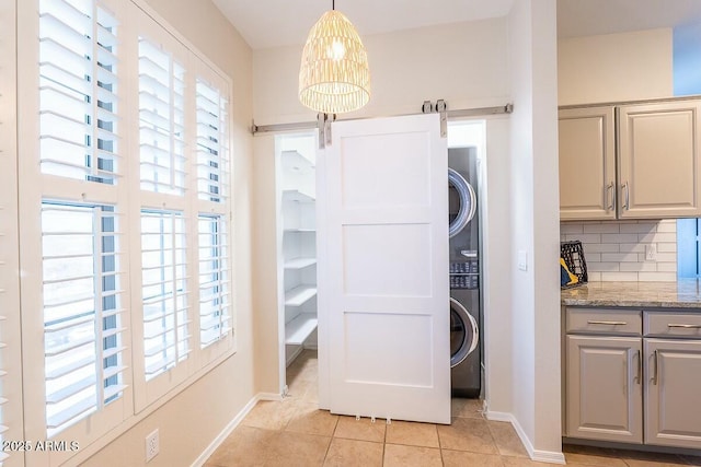 washroom with a barn door, stacked washer / dryer, and light tile patterned flooring