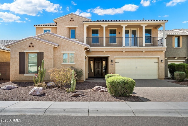 view of front of home featuring stucco siding, a tile roof, decorative driveway, an attached garage, and a balcony