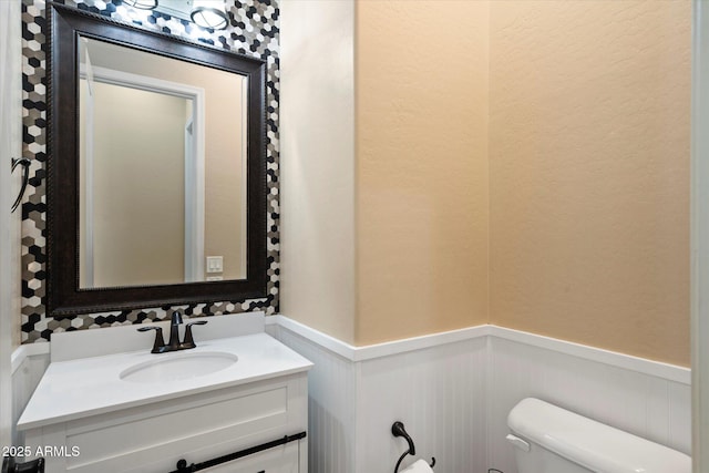 half bathroom with vanity, toilet, and wainscoting