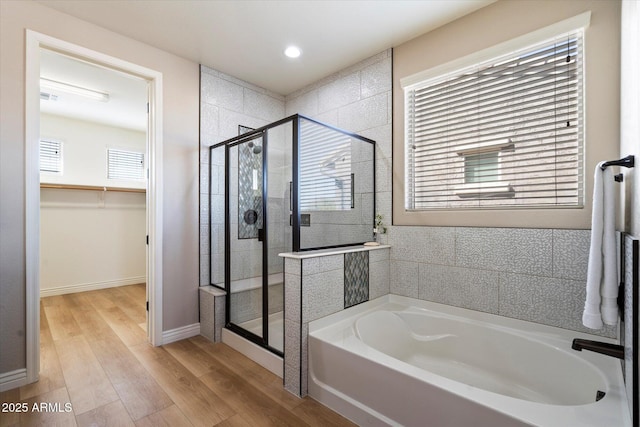 full bath with wood finished floors, plenty of natural light, a stall shower, a spacious closet, and a garden tub