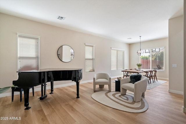 living area with baseboards, visible vents, light wood finished floors, and a chandelier