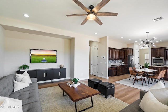 living area with visible vents, ceiling fan with notable chandelier, recessed lighting, light wood finished floors, and baseboards