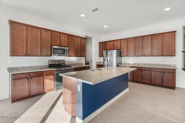 kitchen with a center island with sink, light tile patterned floors, light stone countertops, and appliances with stainless steel finishes