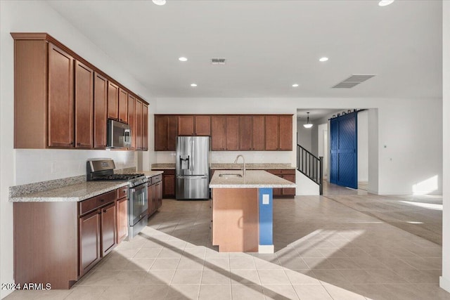 kitchen with a kitchen island with sink, sink, light tile patterned floors, appliances with stainless steel finishes, and light stone counters