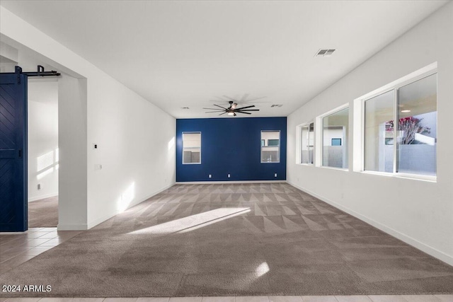 carpeted empty room featuring a barn door, ceiling fan, and a healthy amount of sunlight