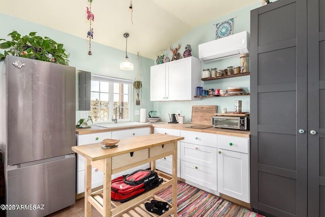 kitchen with white cabinets, freestanding refrigerator, vaulted ceiling, a sink, and a wall mounted AC