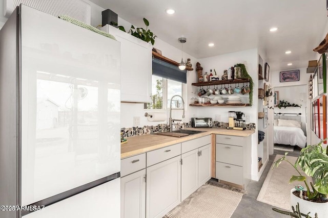 kitchen featuring white cabinets, freestanding refrigerator, light countertops, a sink, and recessed lighting