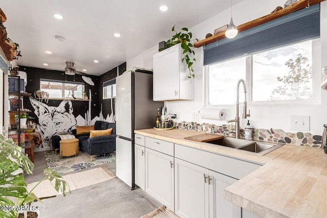 kitchen featuring white cabinets, freestanding refrigerator, a sink, light countertops, and a wealth of natural light