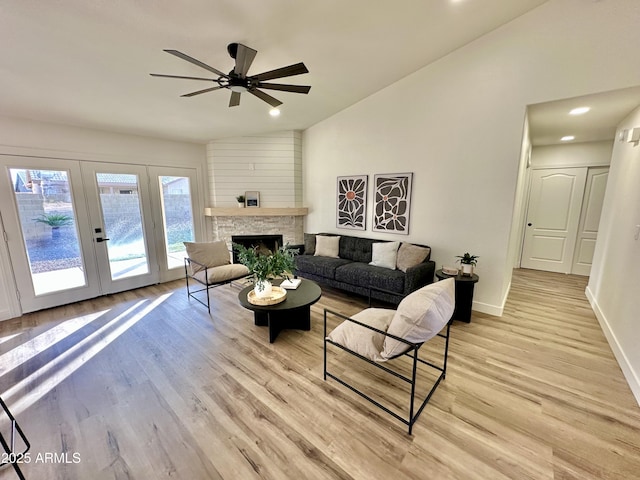 living room featuring a fireplace, lofted ceiling, ceiling fan, light wood-type flooring, and french doors