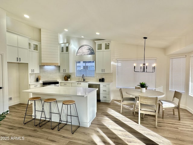 kitchen featuring sink, light hardwood / wood-style flooring, white cabinetry, hanging light fixtures, and a kitchen island