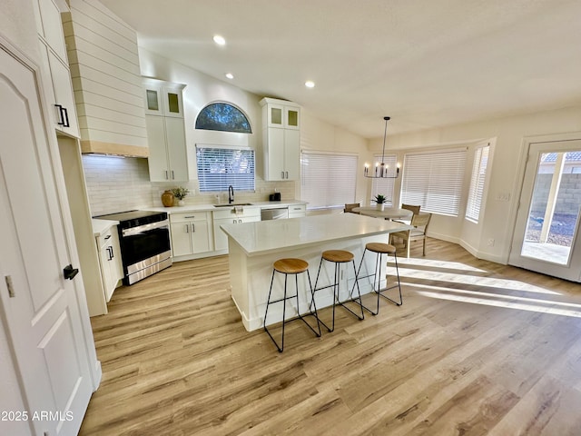 kitchen with decorative light fixtures, a kitchen island, range with electric cooktop, light hardwood / wood-style floors, and white cabinets