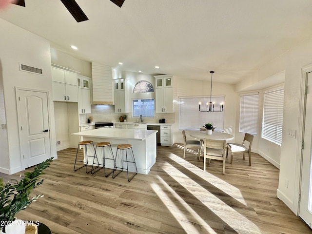 kitchen featuring a kitchen island, white cabinetry, dishwasher, decorative backsplash, and hanging light fixtures