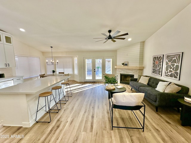 living room featuring french doors, lofted ceiling, light hardwood / wood-style floors, a fireplace, and ceiling fan with notable chandelier