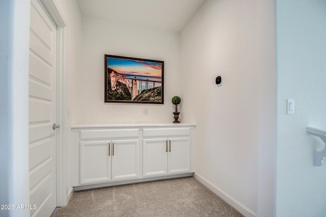 hall featuring light colored carpet and baseboards