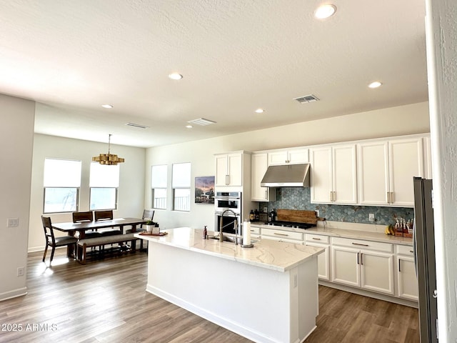 kitchen featuring white cabinetry, sink, tasteful backsplash, an island with sink, and decorative light fixtures