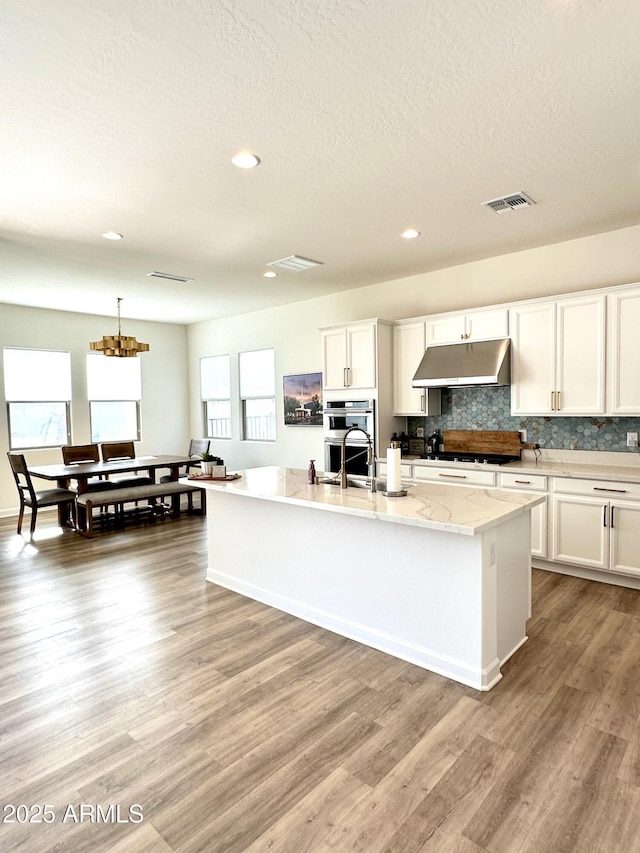 kitchen featuring white cabinets, a center island with sink, double oven, and light hardwood / wood-style floors