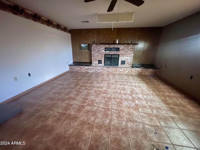 unfurnished living room featuring tile floors, ceiling fan, a brick fireplace, and wooden walls