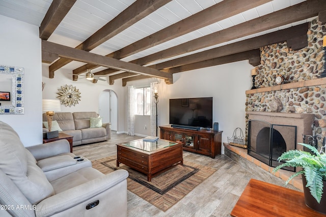 living room with light wood-type flooring, a stone fireplace, and beamed ceiling