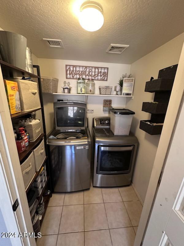 laundry room with washing machine and clothes dryer, a textured ceiling, and light tile patterned floors