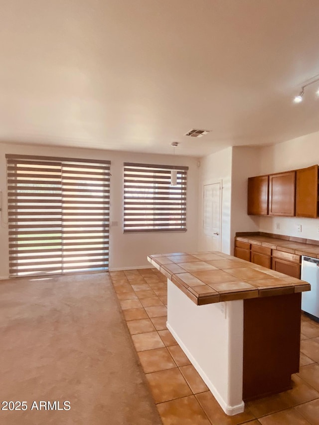 kitchen with tile counters, light tile patterned flooring, a breakfast bar area, and dishwashing machine