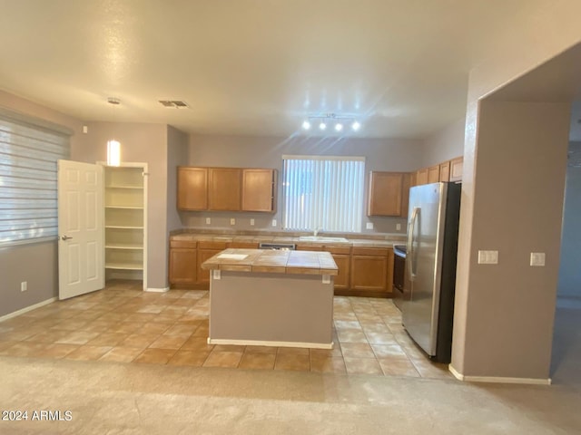 kitchen with appliances with stainless steel finishes, sink, light tile patterned floors, a center island, and tile counters