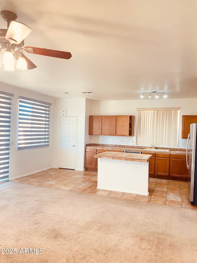 kitchen with stainless steel refrigerator, hanging light fixtures, a kitchen island, and light tile patterned flooring