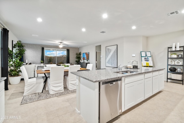 kitchen with sink, dishwasher, light stone countertops, white cabinets, and a center island with sink