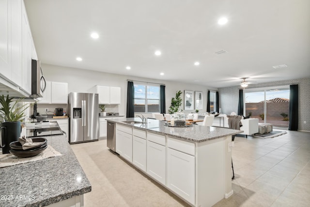 kitchen featuring a kitchen island with sink, light stone countertops, stainless steel appliances, and white cabinets