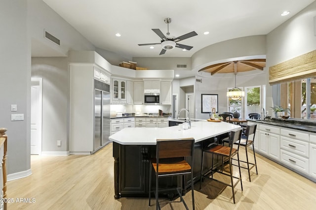 kitchen featuring visible vents, white cabinets, a large island, built in appliances, and light wood-type flooring