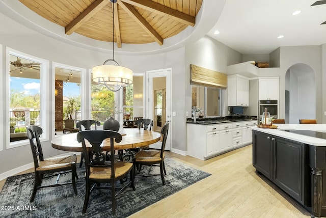 dining room featuring arched walkways, light wood-type flooring, wooden ceiling, and beam ceiling