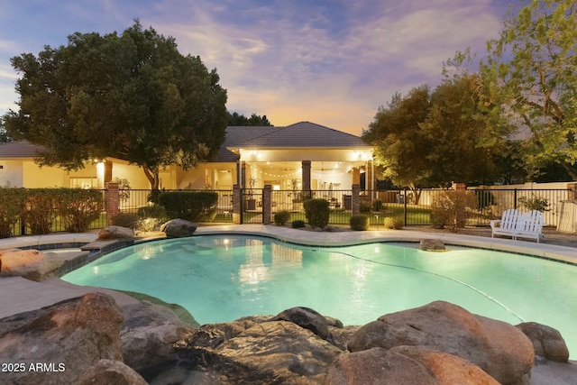 pool at dusk featuring fence and a pool with connected hot tub