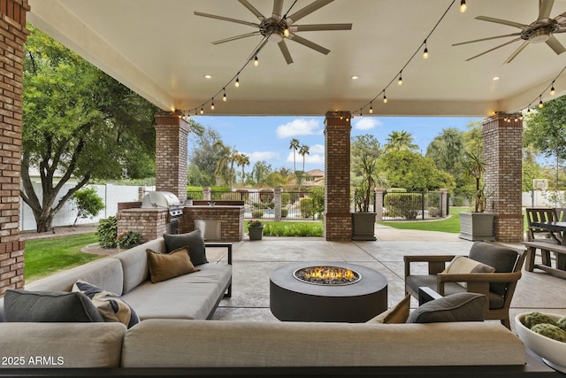 view of patio / terrace with an outdoor living space with a fire pit, a grill, fence, ceiling fan, and exterior kitchen